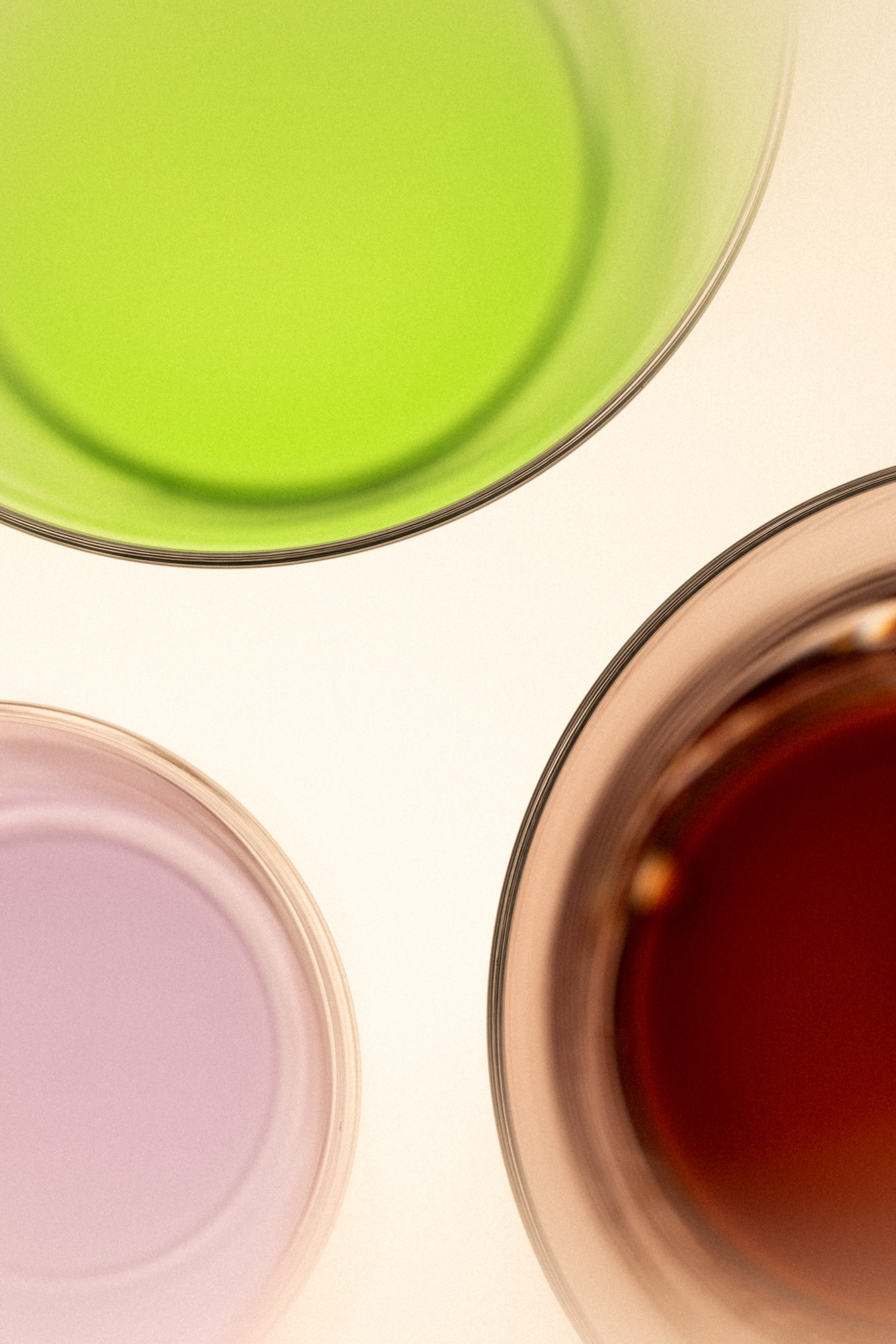 Three glasses seen from above, filled with green, lilac and deep red drinks